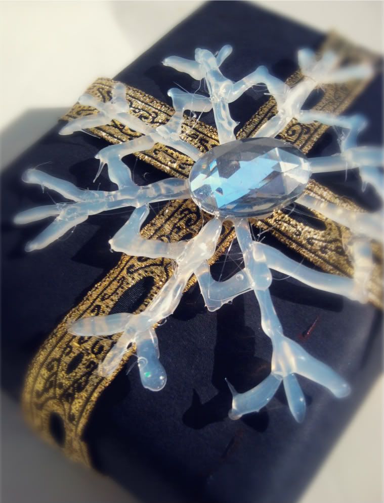 DIY hot glue white snowflake ornament on top of black gift wrap and ornate Christmas ribbon