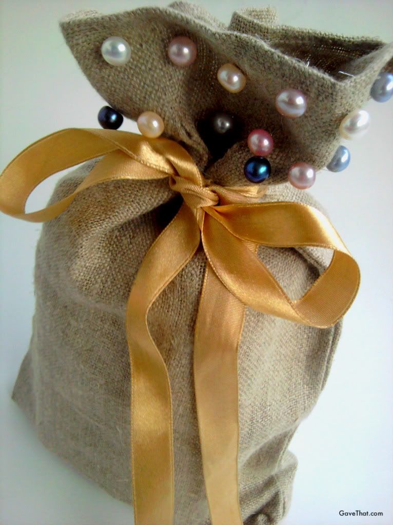 Pearl earrings on a burlap gift bag tied with a ribbon bow
