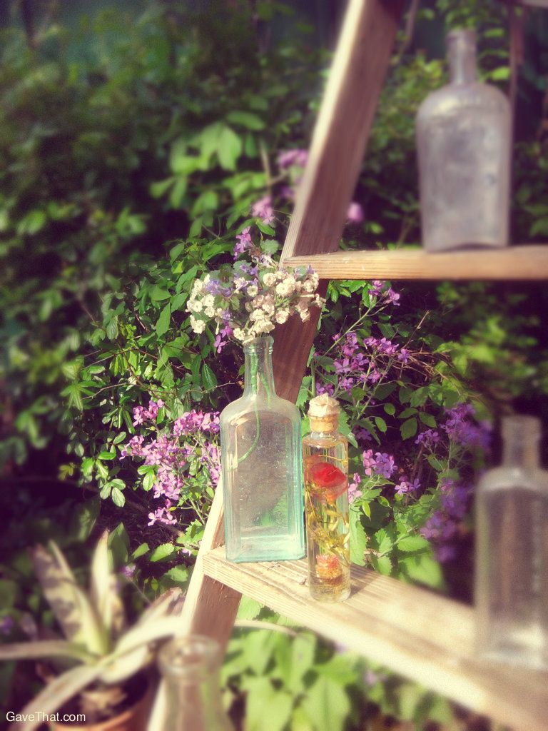 Antique glass bottles filled with flowers and floral oils on an old wooden ladder