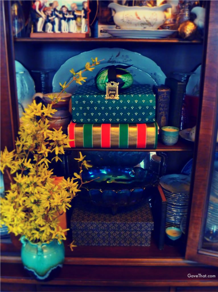 Sprucing up a book case china closet with wrapped gifts and left over gift boxes in green with golden Forsythia flowers